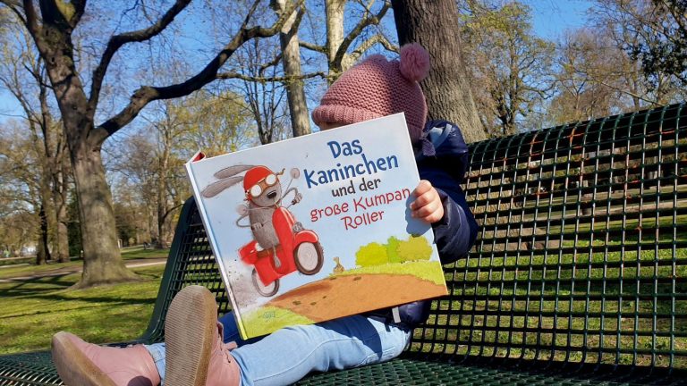 Kind auf einer Parkbank mit Kinderbuch in den Händen